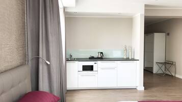 A modern hotel room with a bed, a small kitchenette, and a bathroom visible in the background.