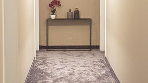 A narrow hallway with a textured floor, a small table with decorative items, and wall-mounted lights. - TH39 Trend Hotel (Bad Vilbel)