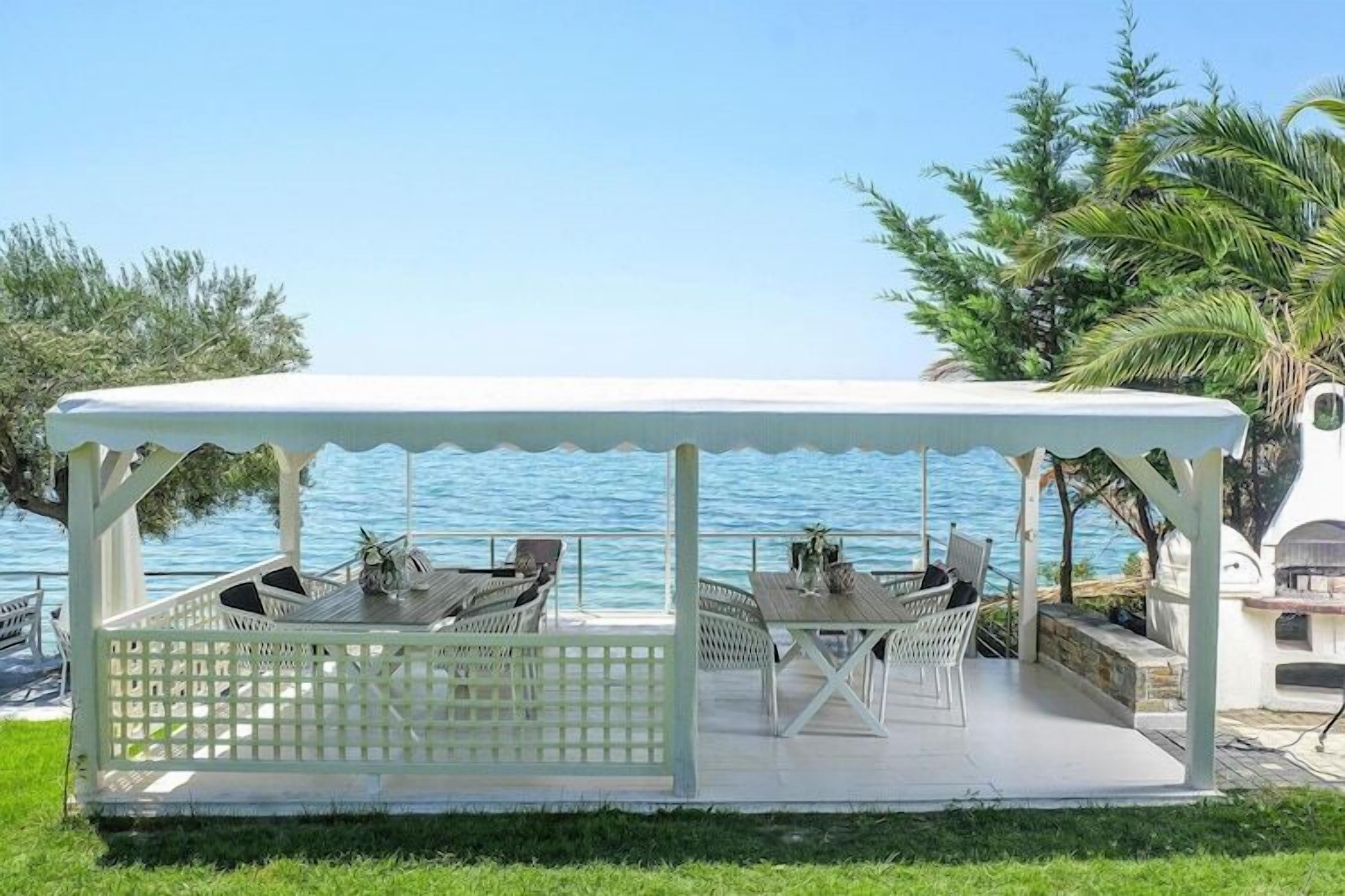 A covered outdoor seating area with tables and chairs, overlooking a body of water.