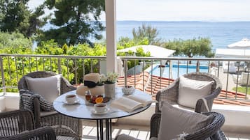 Un balcone con mobili in vimini, un tavolo con un libro, una tazza e un piatto di cibo, con vista su una piscina e uno specchio d'acqua.