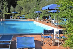 Una piscina amb gandules i ombrel ·les, envoltada de vegetació.