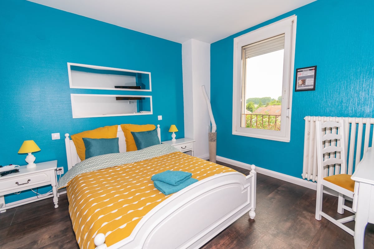 Een slaapkamer met een bed, nachtkastjes, een stoel, een raam en uitzicht op buiten.
