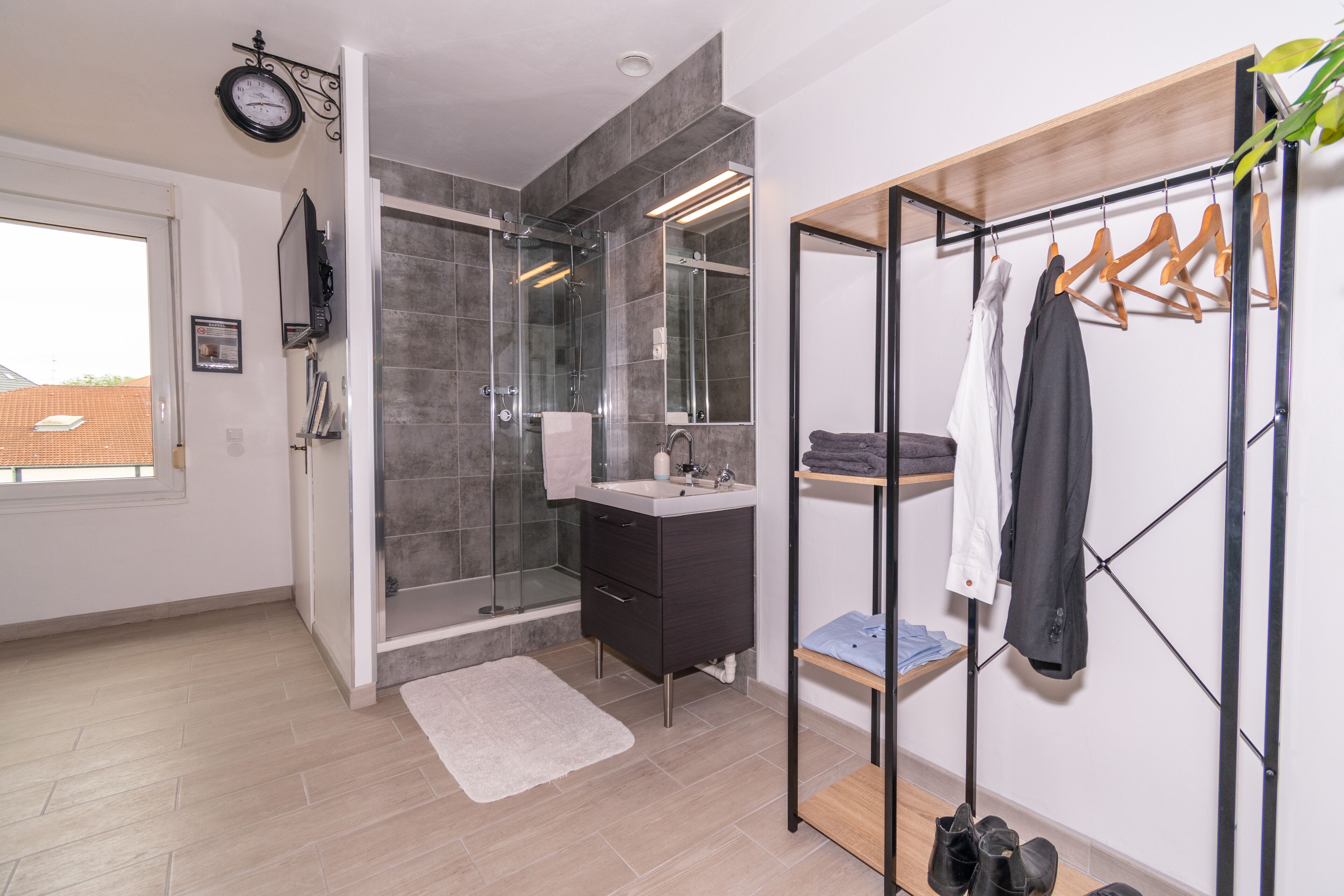 A modern bathroom with a glass shower, a vanity, and a clothing rack.