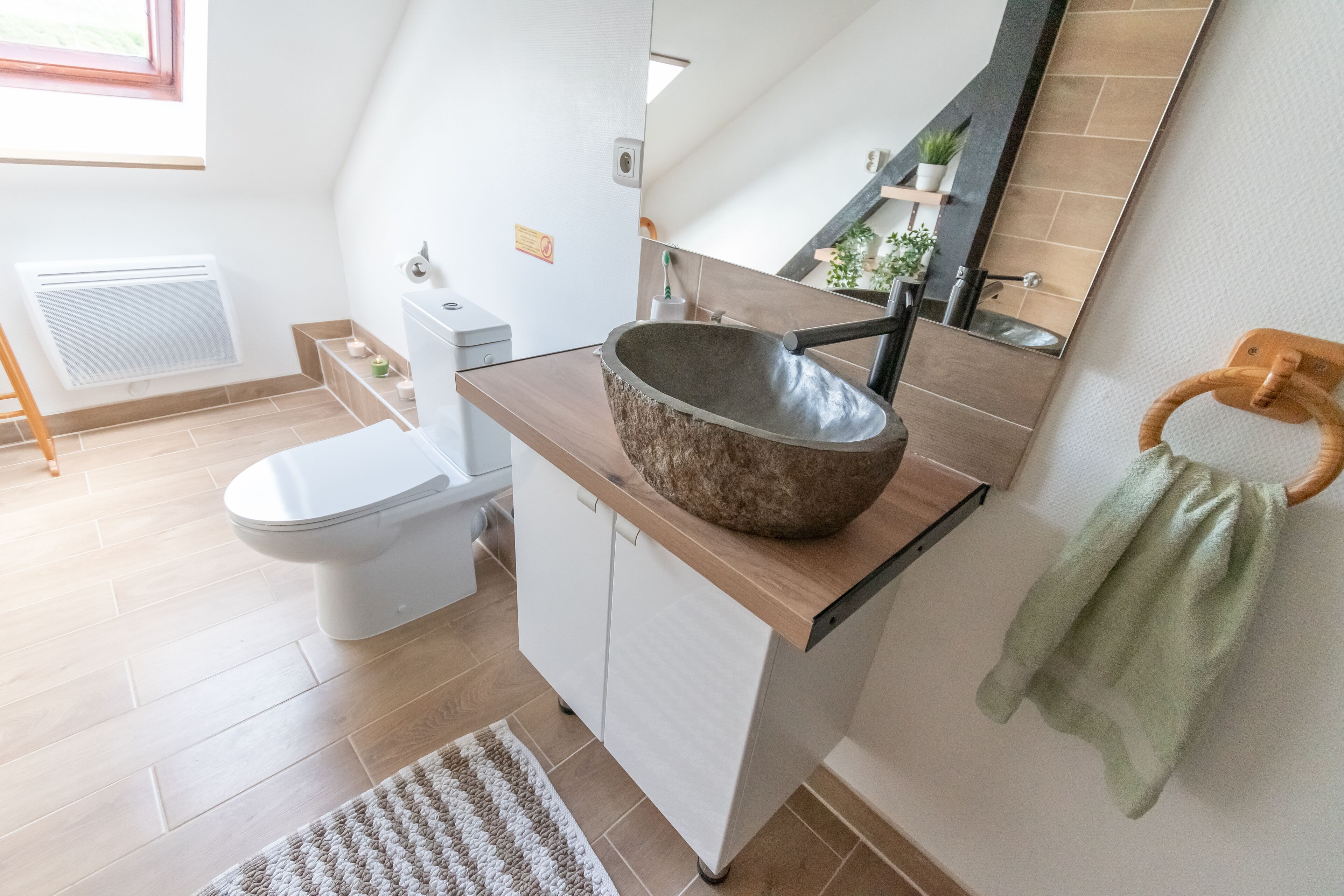 Un baño moderno con un inodoro blanco, un tocador de madera con un lavabo grande, un perchero y un espejo.