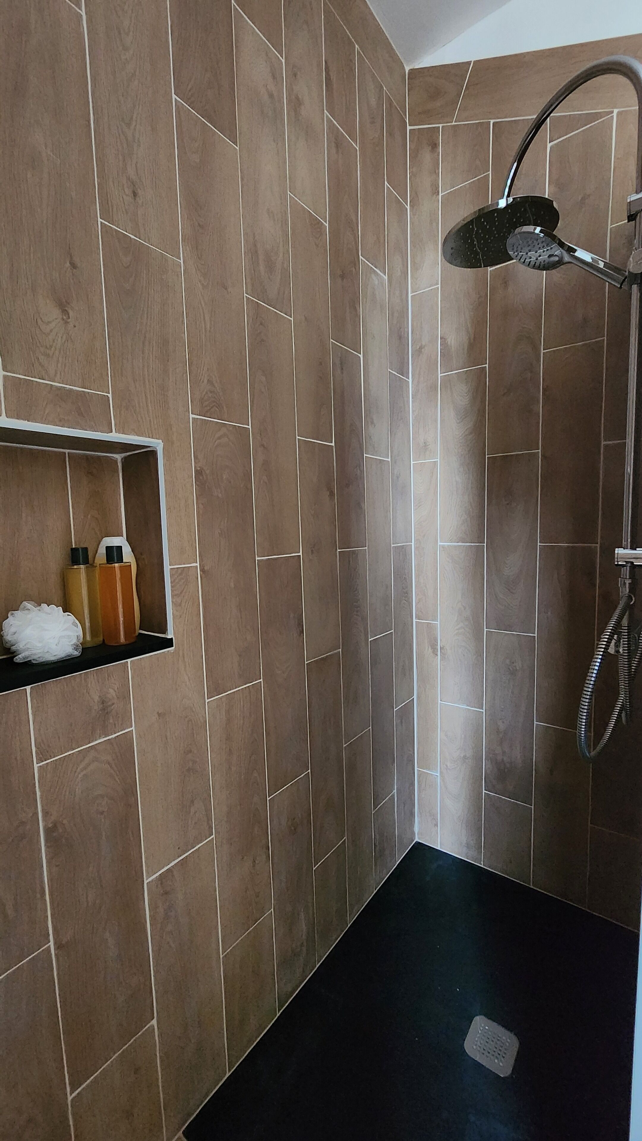 A shower area with a wooden wall design, a shelf with toiletries, and a showerhead.