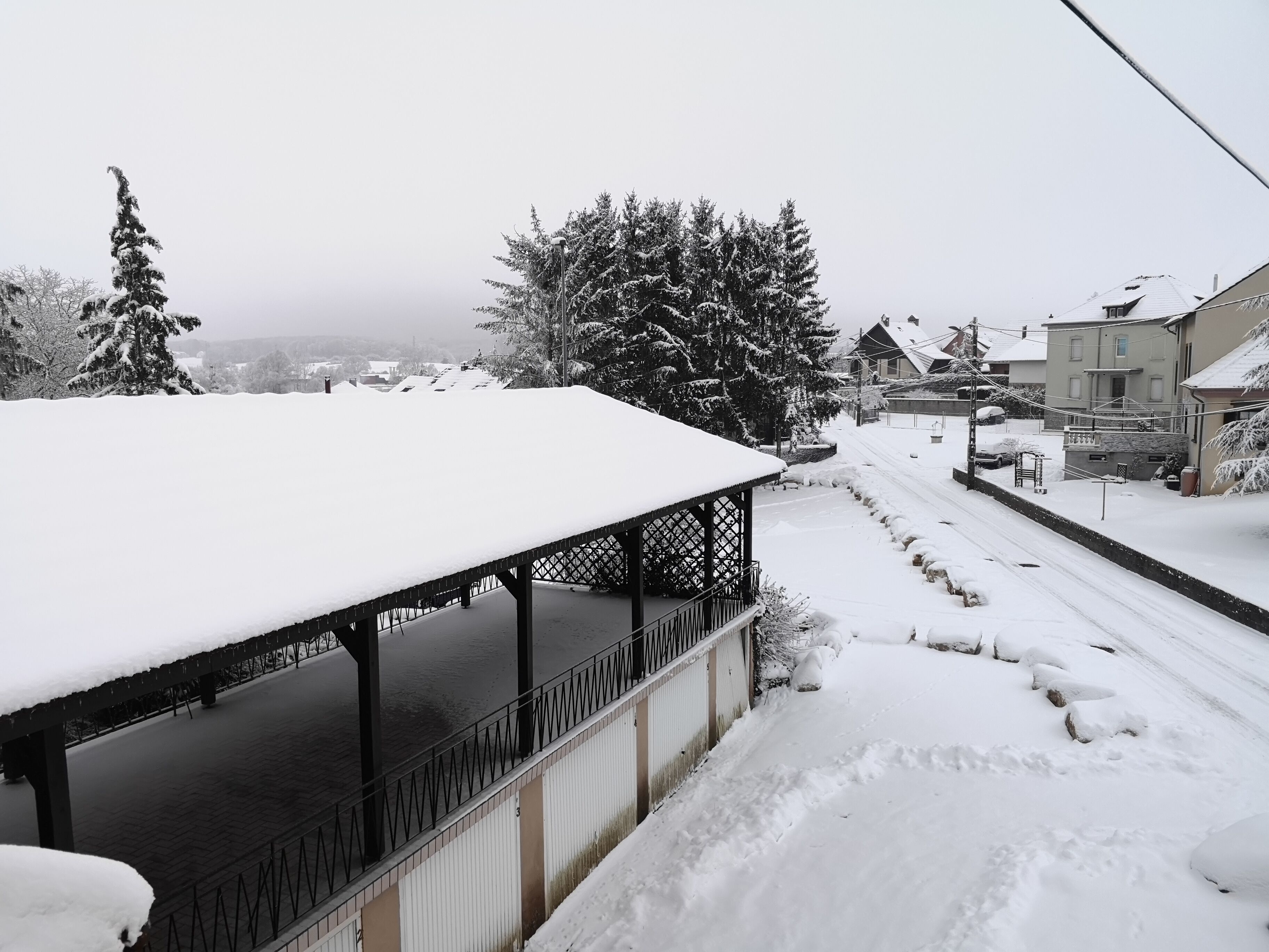 A covered outdoor area with a snow-covered roof, a metal railing, and a snow-covered ground.