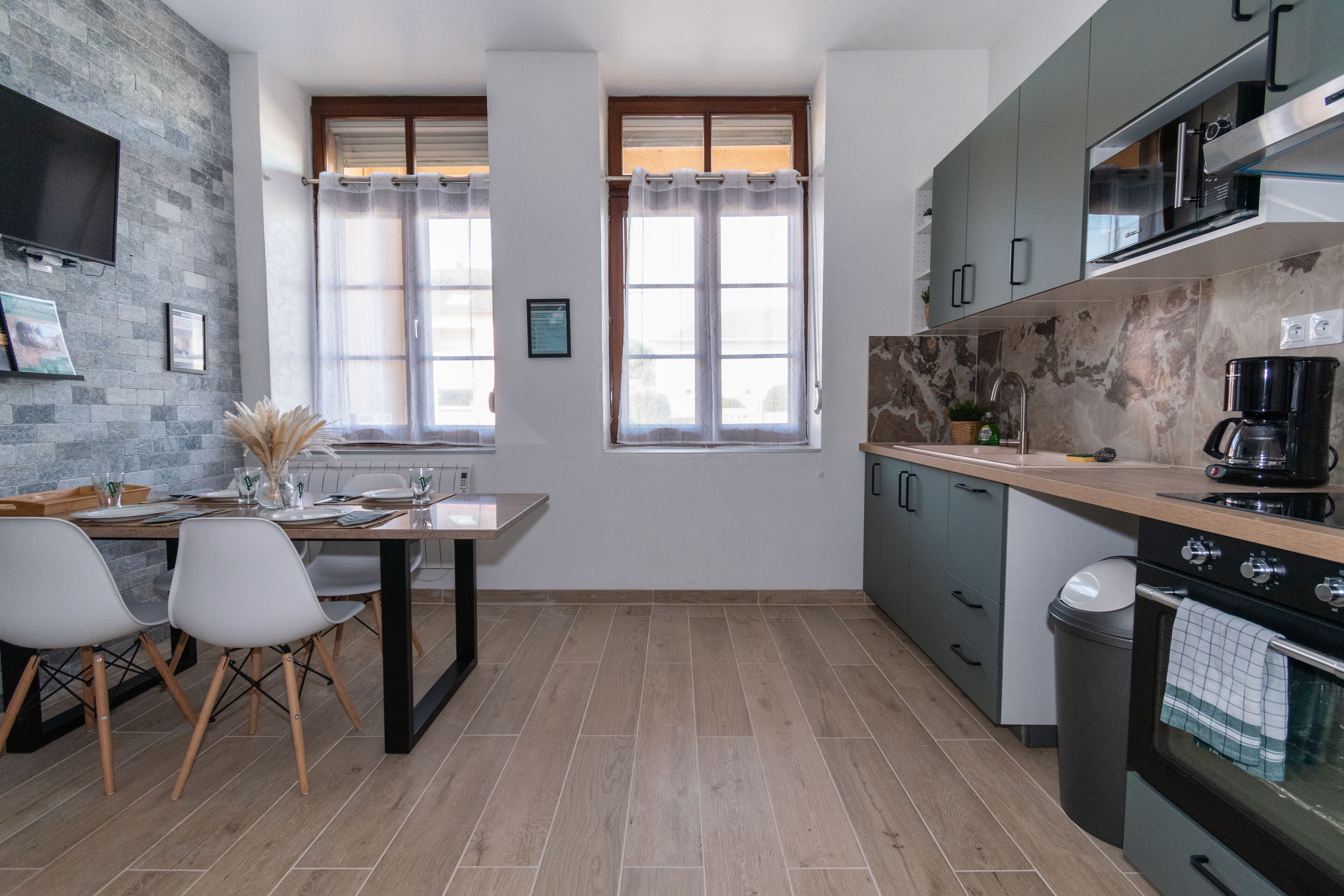 A modern kitchen with a dining area, featuring a stone wall, wooden flooring, and contemporary appliances.