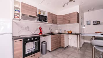 A modern kitchen with wooden cabinets, a black microwave, a coffee maker, and a trash can.