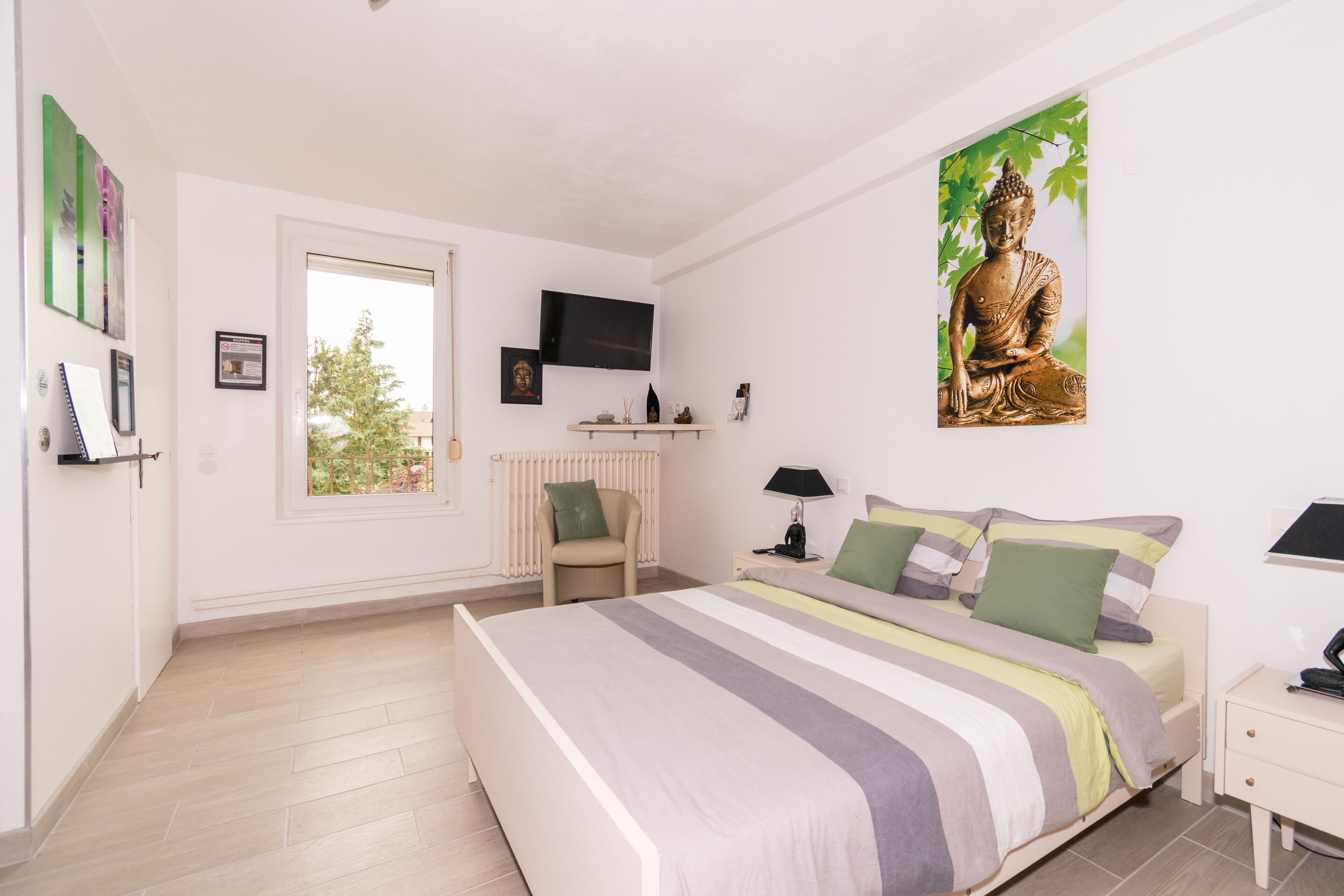 A bedroom with a large bed, a TV mounted on the wall, a window, and a Buddha statue.