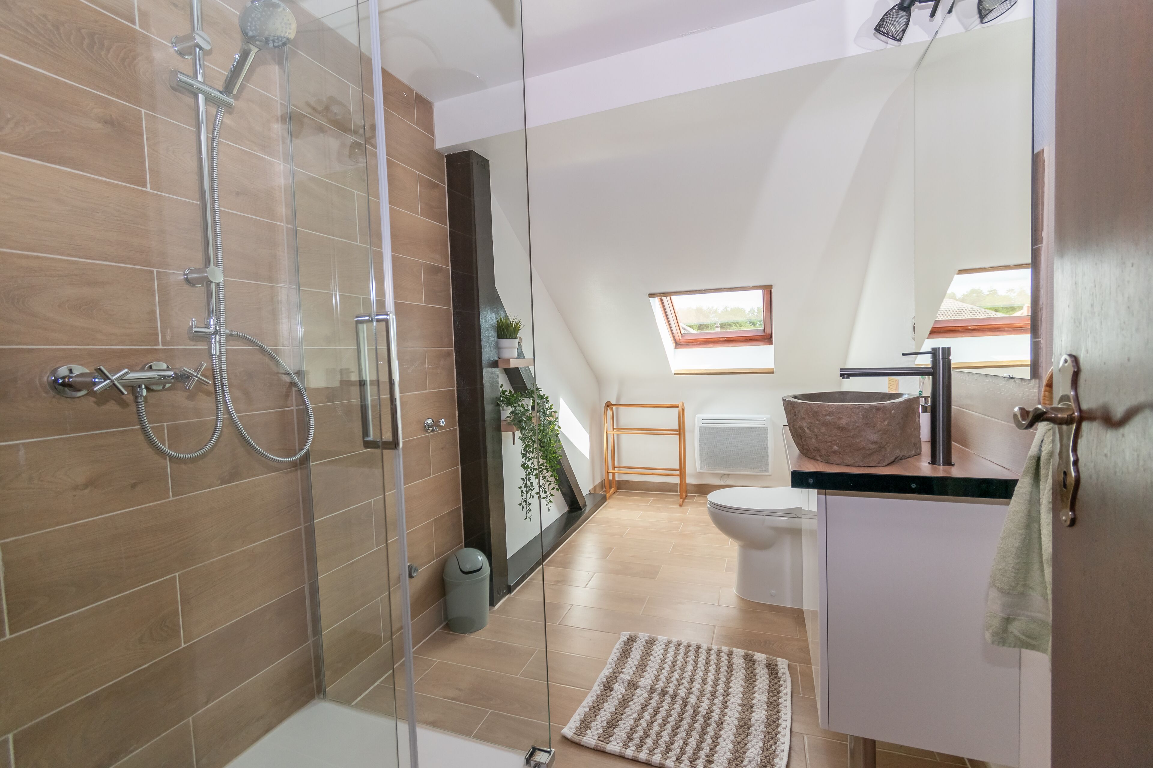 A modern bathroom with a glass-enclosed shower, a freestanding toilet, and a large mirror.