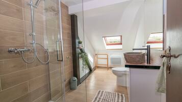 A modern bathroom with a glass-enclosed shower, a freestanding toilet, and a large mirror.