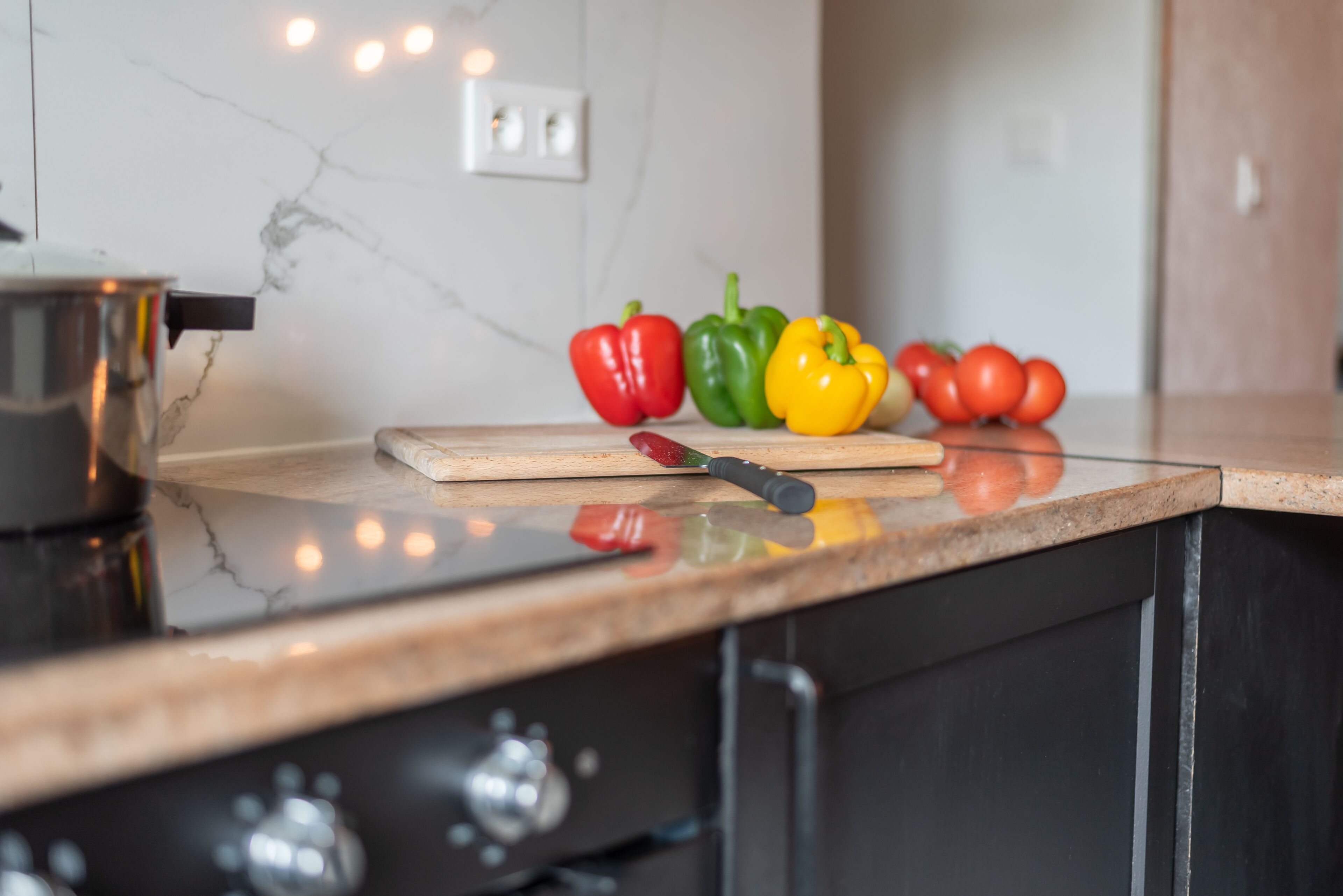Una encimera de cocina con tabla de cortar, un cuchillo y pimientos de colores.