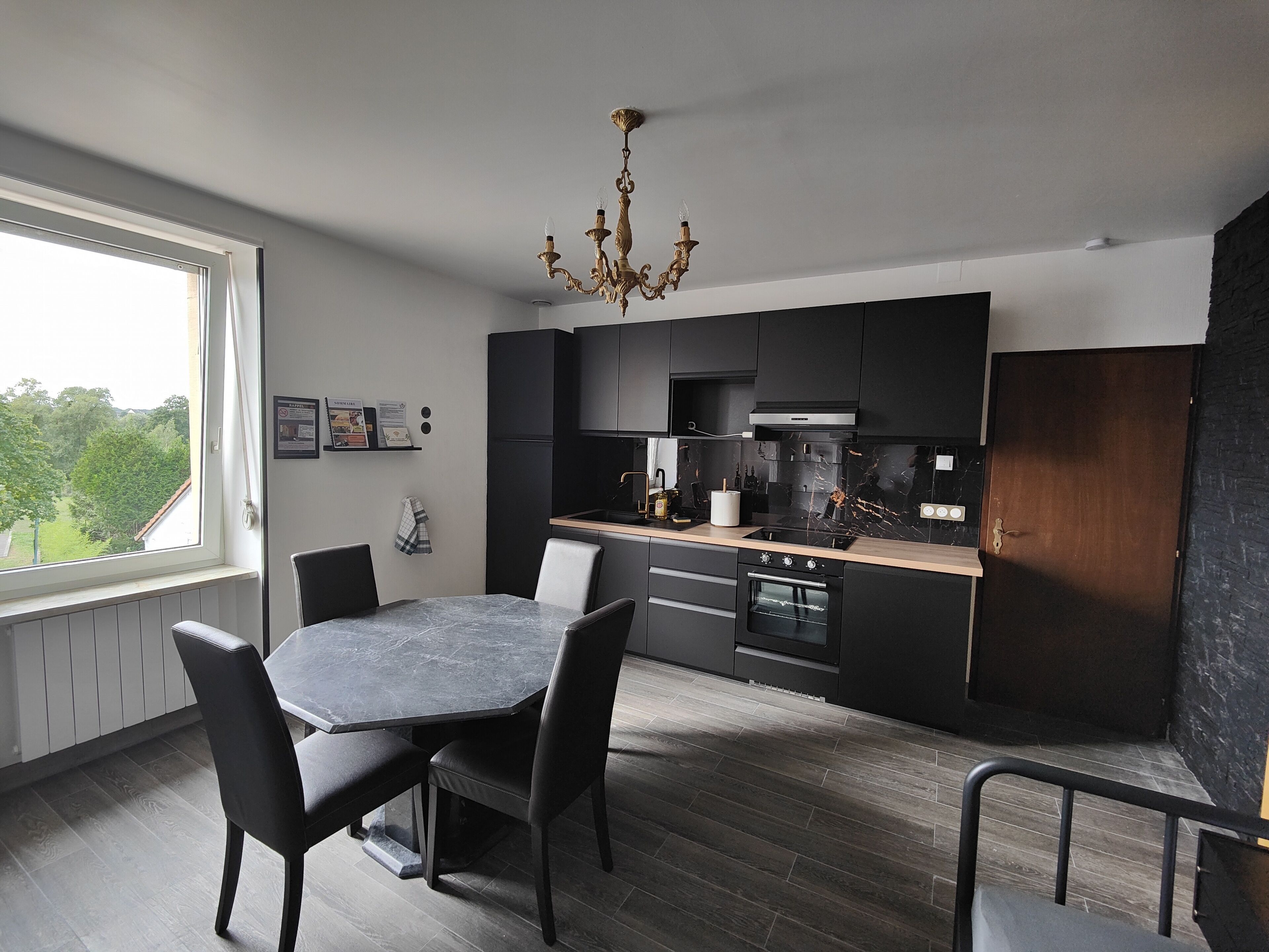 Una cocina moderna con armarios oscuros, encimera de mármol y comedor con mesa y sillas.
