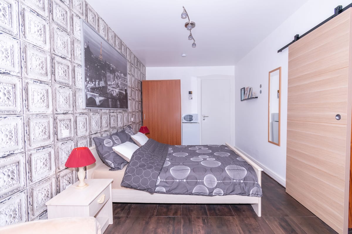 Een slaapkamer met een bed, een nachtkastje, een rode lamp, een houten garderobe en een wand met behang.