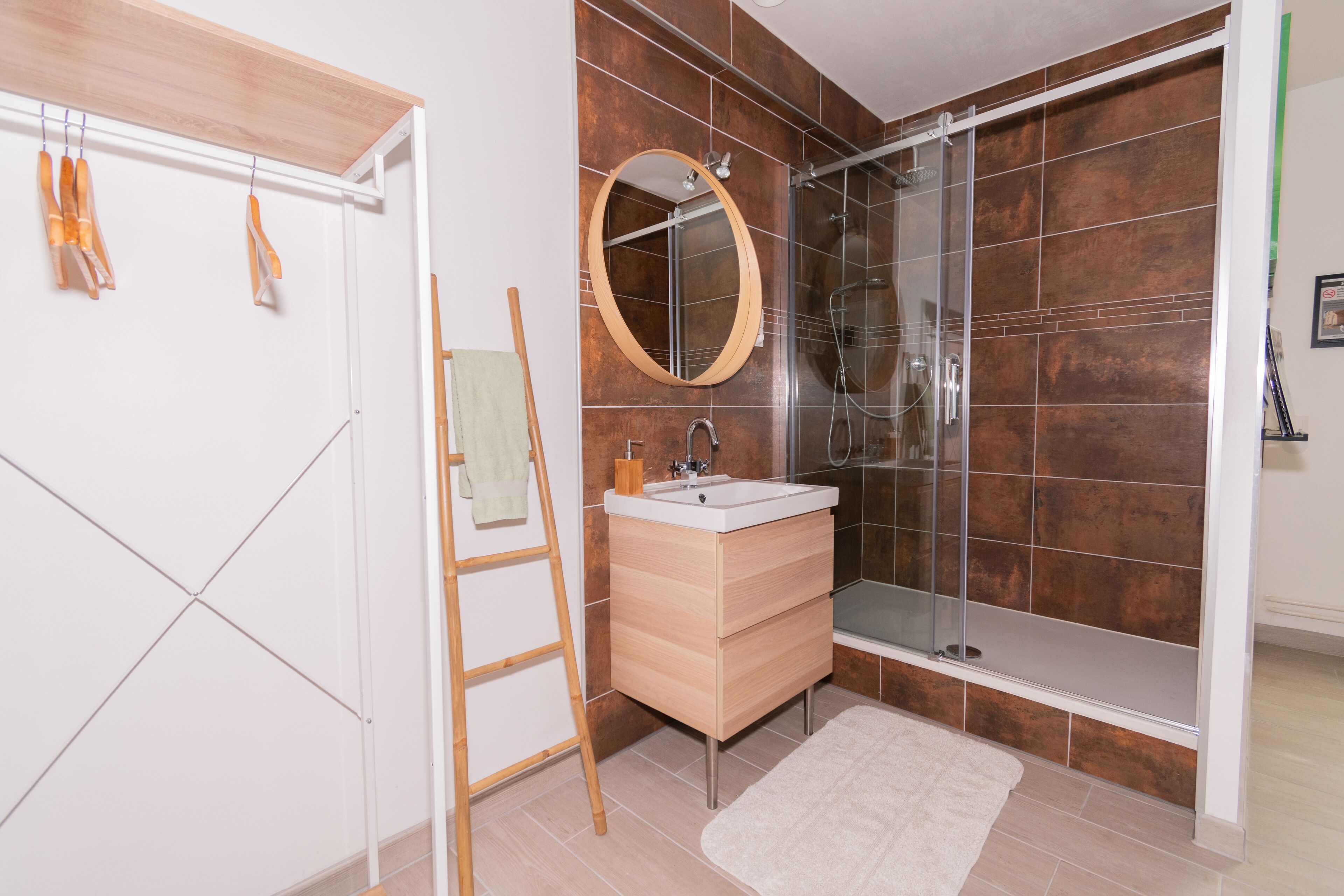 A bathroom with a wooden vanity, a round mirror, a glass shower enclosure, and a white towel hanging on a rack.