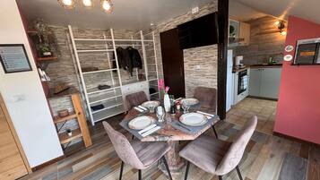 A dining area with a wooden table set for four, surrounded by cushioned chairs. A white cabinet with a glass top is visible to the left.