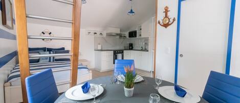 Un comedor con una mesa dispuesta para cuatro, sillas azules y una cocina al fondo.