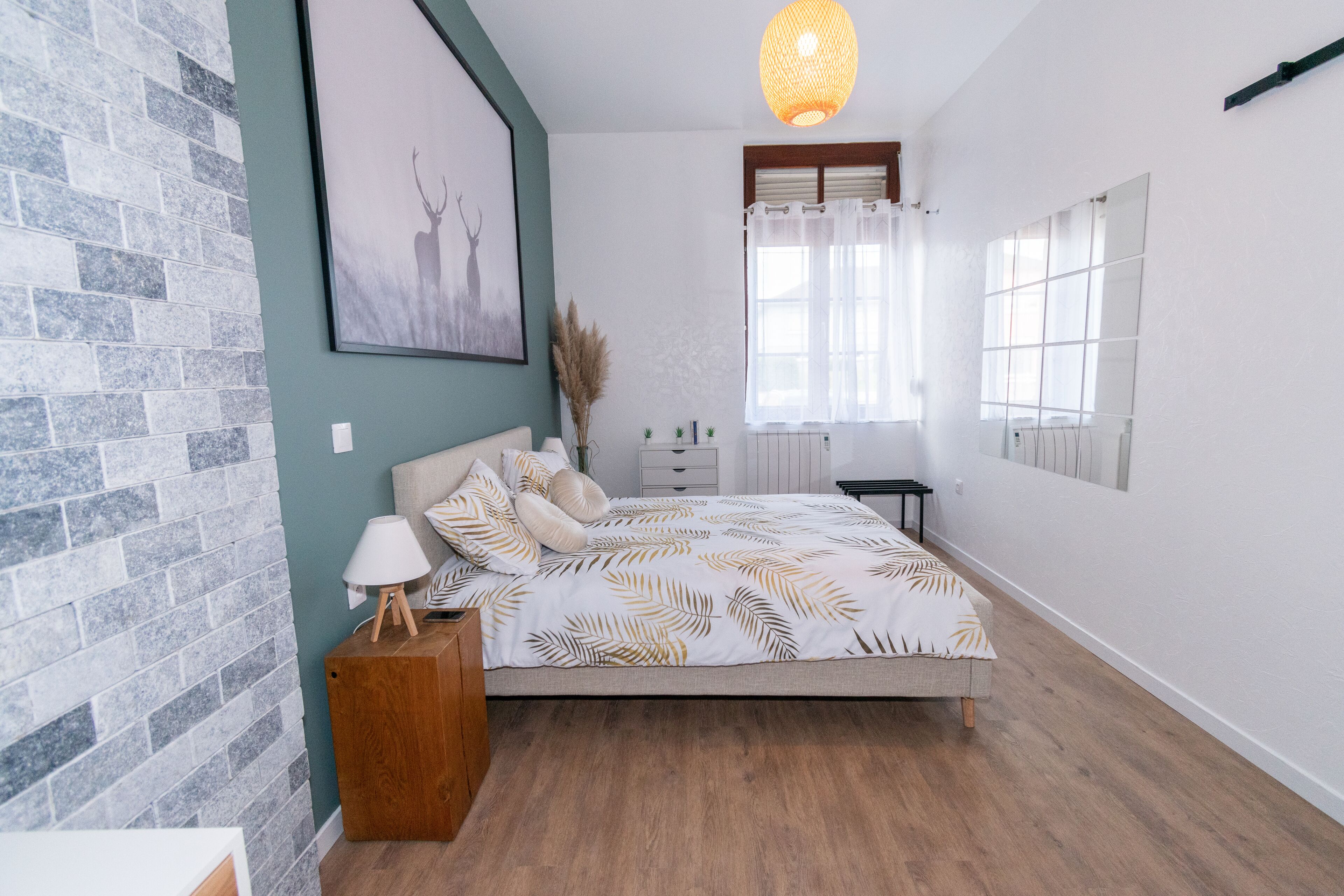 Un dormitorio moderno con una cama grande, una mesita de noche, una lámpara y una ventana con cortinas.