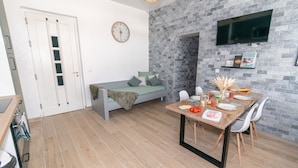 Une pièce de taille modeste comprenant un lit, une table à manger pour deux personnes, un téléviseur fixé au mur et une horloge également fixée au mur.