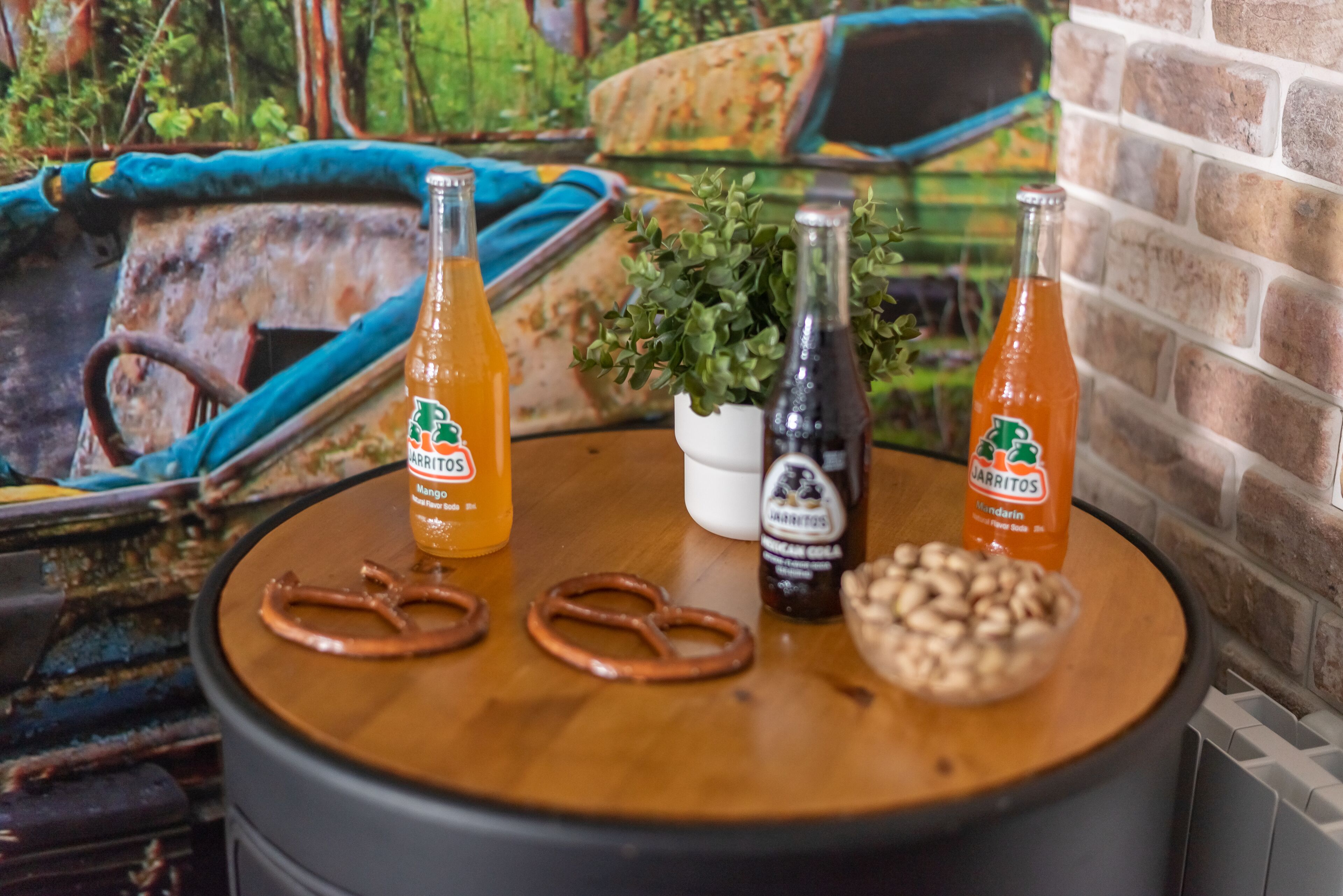 A table with two bottles of 'JARITOS' drink, two pretzels, a small bowl of nuts, and a potted plant.