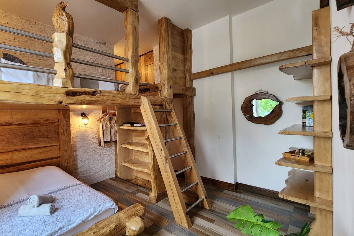 Een eenvoudige kamer met houten wanden, een stapelbed, een ladder en een klein houten plankje.