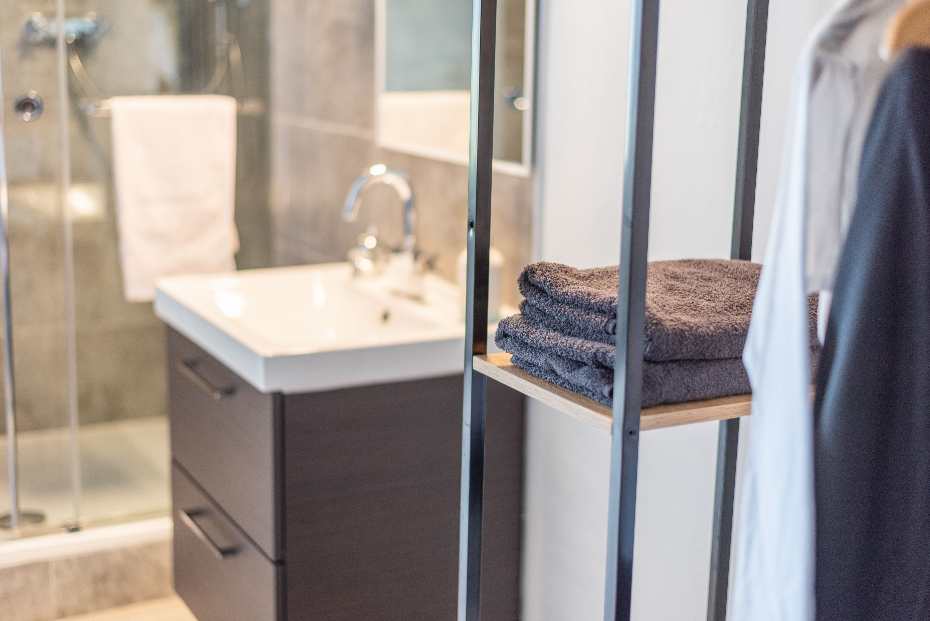 A modern bathroom with a glass shower enclosure, a white sink, and a towel rack with folded towels.