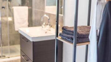 A modern bathroom with a glass shower enclosure, a white sink, and a towel rack with folded towels.