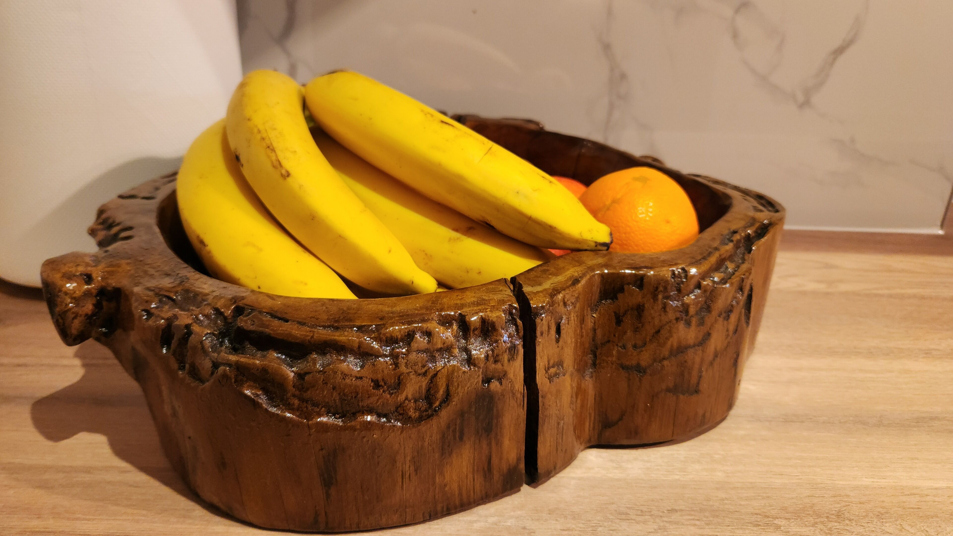 Un saladier en bois contenant des bananes et une orange, posé sur une surface en bois.