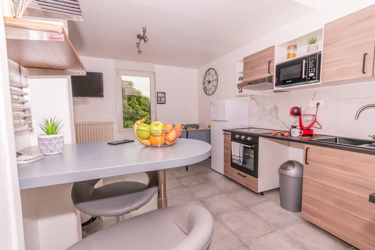 Een moderne keuken met een inbouwoven, magnetron en spoelbak. Er staat een eettafel met stoelen en een schaal met fruit.