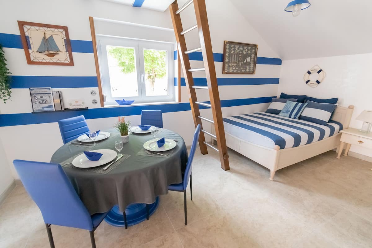 Een kamer met een bed, een eettafel met stoelen, een raam en een ladder.