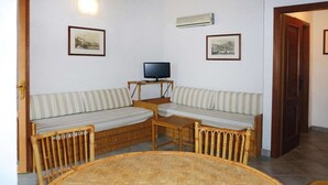 A room with a round wooden table, two striped sofas, a television on a wooden stand, and two framed pictures on the wall.