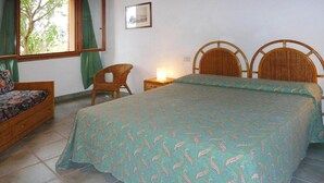 A bedroom with a bed, a chair, a bedside table with a lamp, and a window with curtains.