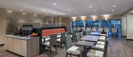 A modern restaurant with a central island, multiple seating areas, and large windows offering views.