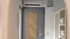 Un passadís amb una porta gris, un estriat tapet de porta, una prateleira blanca amb tovalloles, i una làmpada penjant.