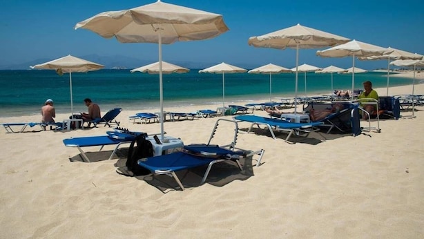 Una platja amb files de gandules i ombrel·les, un cel blau clar i l'oceà al fons.