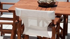 Taula de fusta amb un drap blanc i un centre de pedra, amb vista a una platja plena de papereres i palmeres.