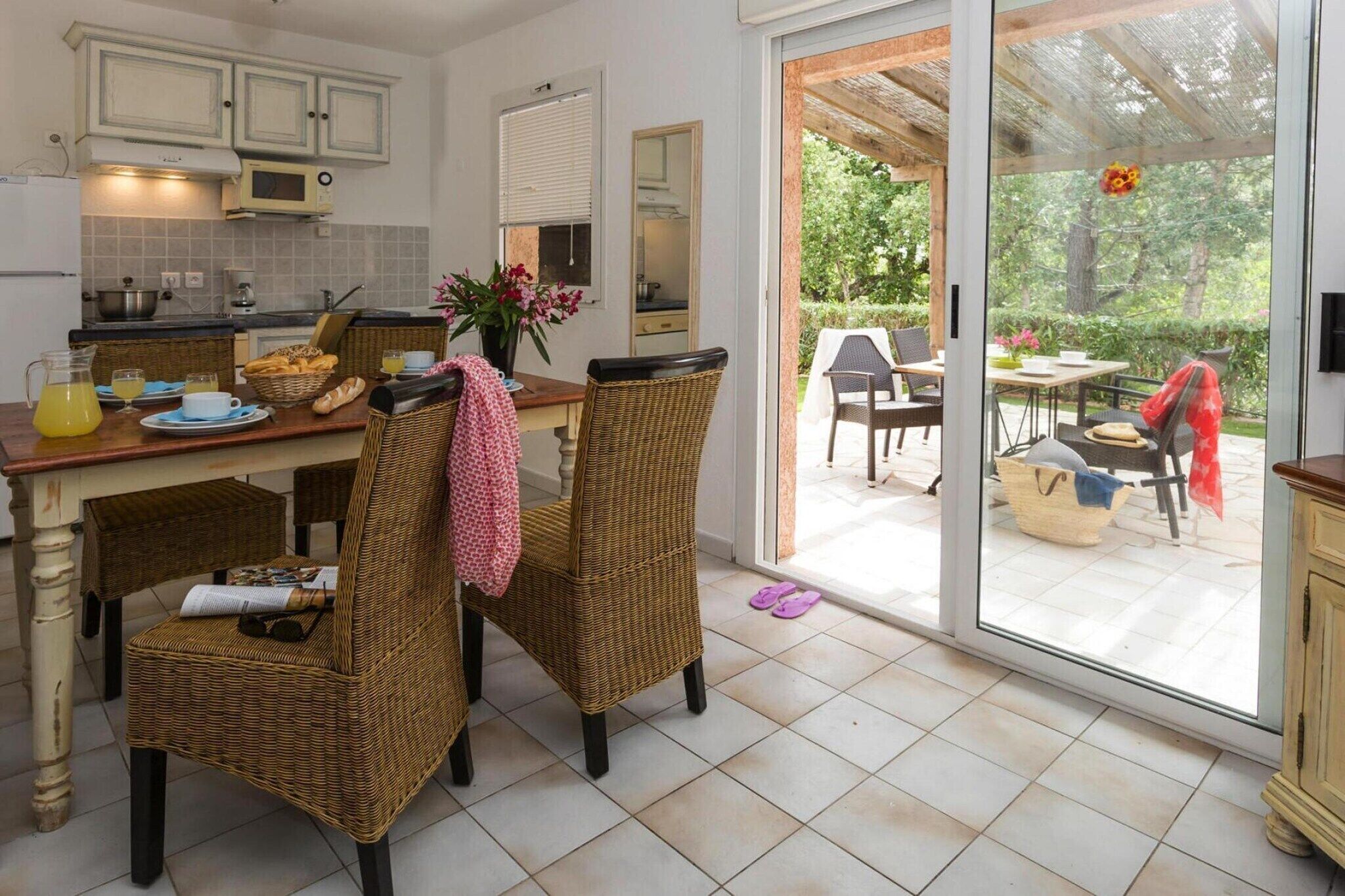Una cocina con sillas de mimbre, una mesa de comedor y vista al jardín a través de un ventanal.