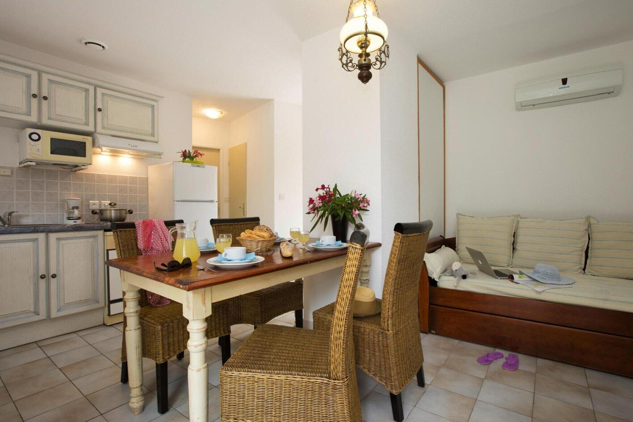 Una cocina con una mesa de comedor, sillas de mimbre, un refrigerador y un microondas.