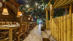 A restaurant with wooden tables and chairs, hanging lights, and a brick wall. - Treebo Dreamland Guest House (Barasat)