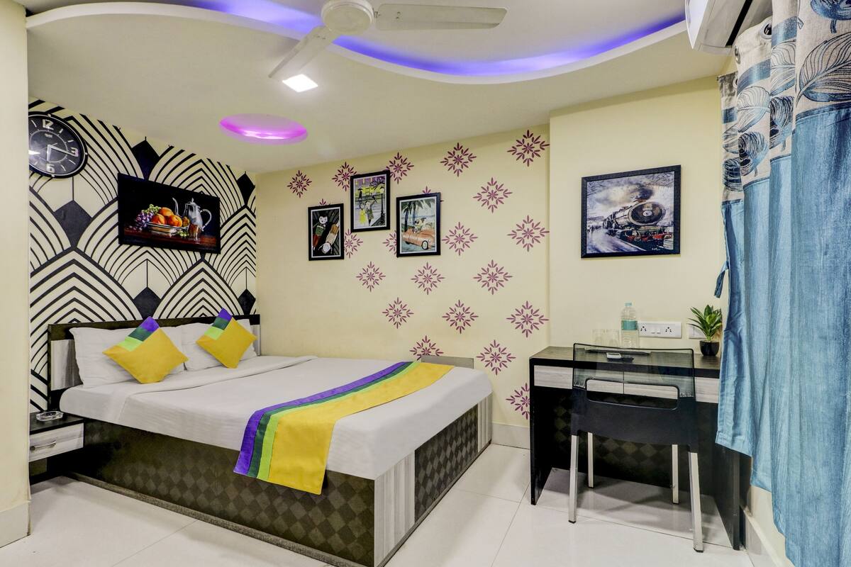 A bedroom with a bed, a desk, and a chair. There are wall decorations and a ceiling fan.