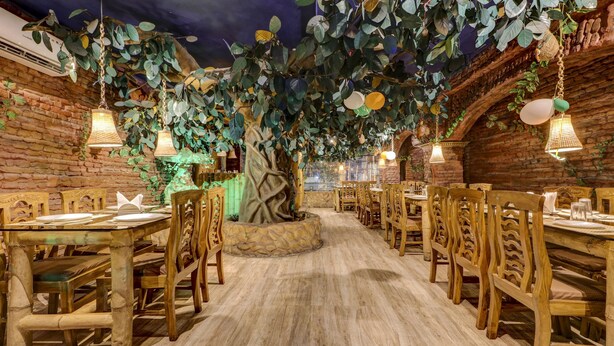 A restaurant with wooden tables and chairs, hanging plants, and brick walls. - Treebo Dreamland Guest House (Barasat)