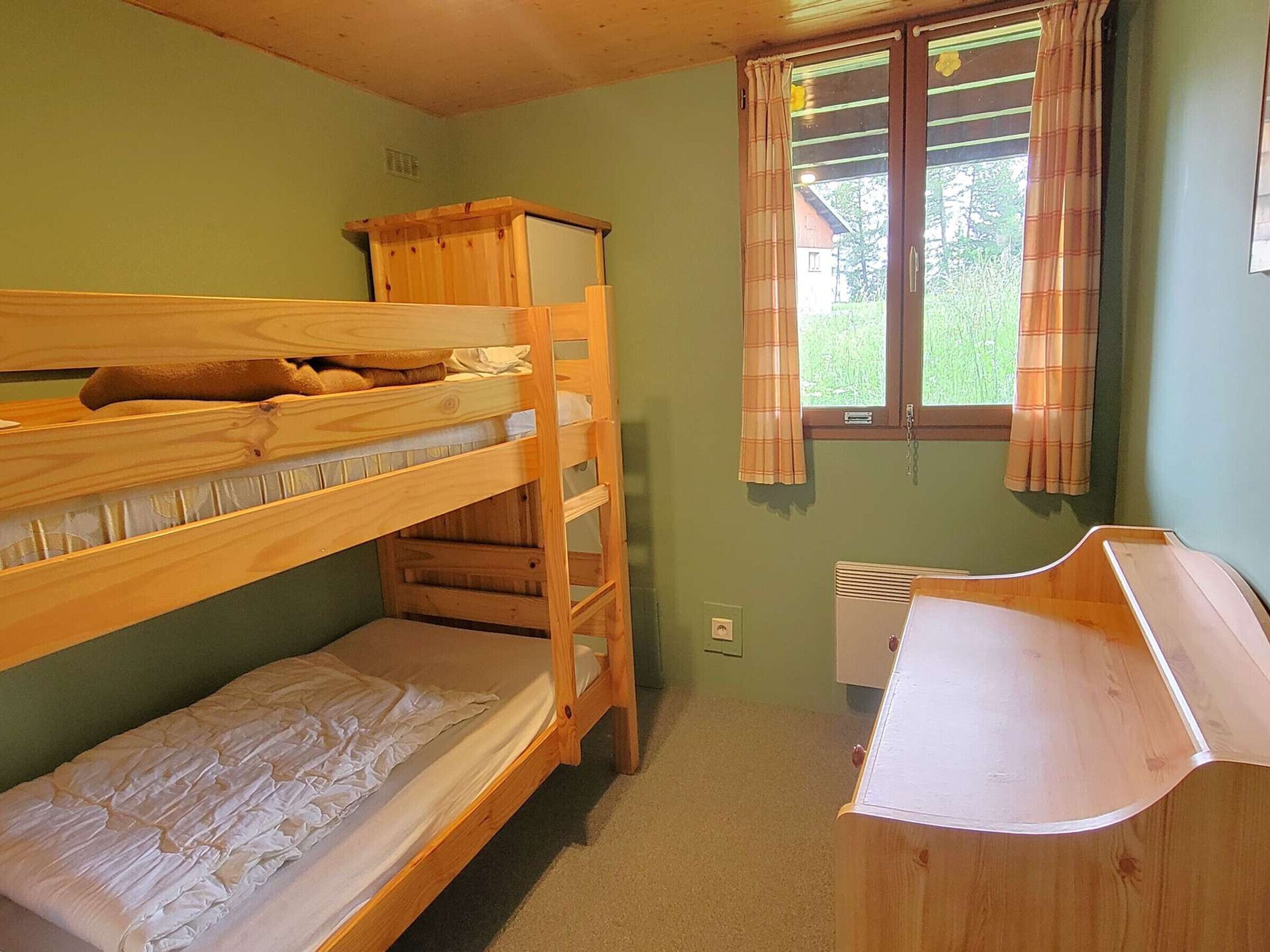 A bunk bed room with a desk and a window with curtains.