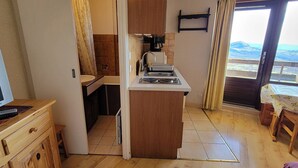A compact kitchen with a sink, stove, and a small dining area with a table and chairs. - Studio for 2 with south-facing balcony, near station (Saint-Michel-de-Chaillol)