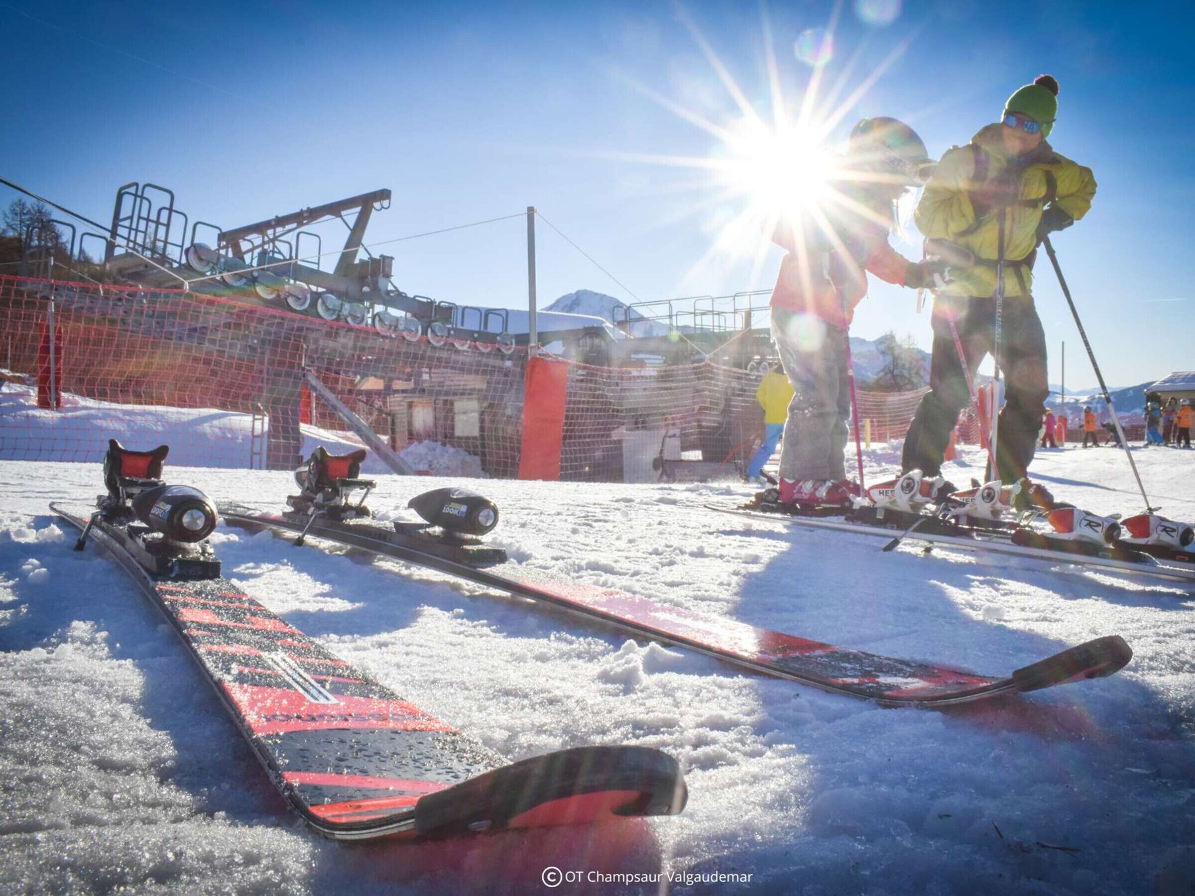 A ski slope with a netted fence, a ski lift, and a skier in the background.