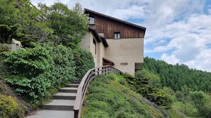 A modern two-story building with a stone staircase leading up to a wooden deck. - Studio for 2 with south-facing balcony, near station (Saint-Michel-de-Chaillol)