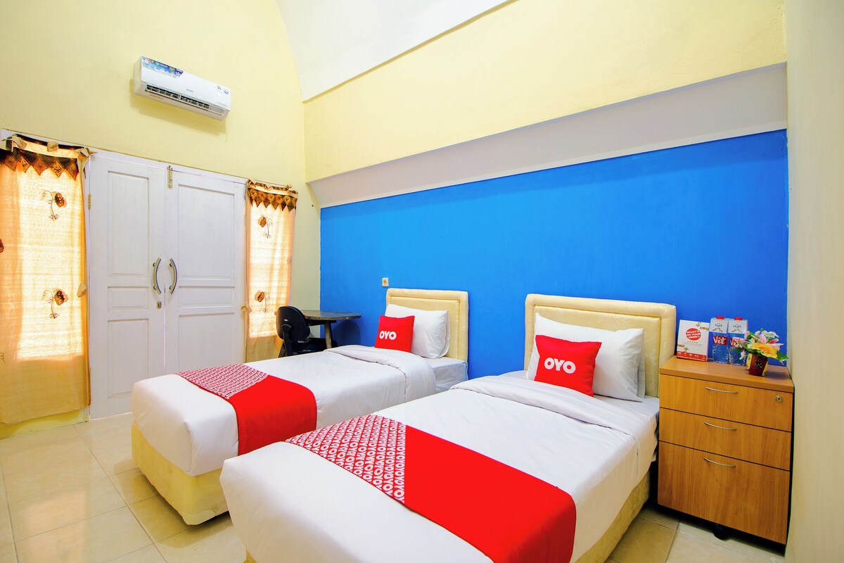Une chambre d’hôtel avec deux lits, un bureau, une chaise, une armoire et une table de chevet avec une lampe.