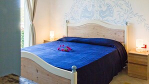 A bedroom with a bed, two bedside tables, a wall with a floral pattern, and a window with curtains. - Apartment in Golfo Aranci with terrace (Baja Sardinia (SS))