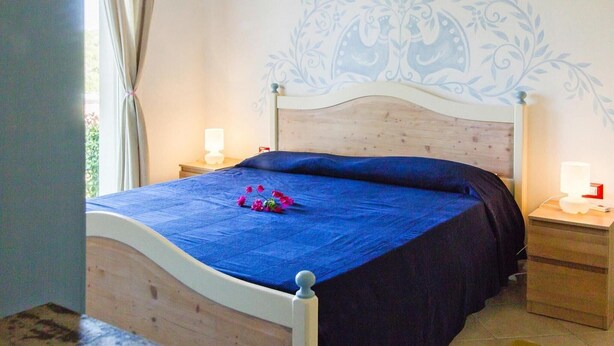 Une chambre à coucher avec un lit, deux tables de chevet, un mur orné d’un motif floral et une fenêtre avec des rideaux.