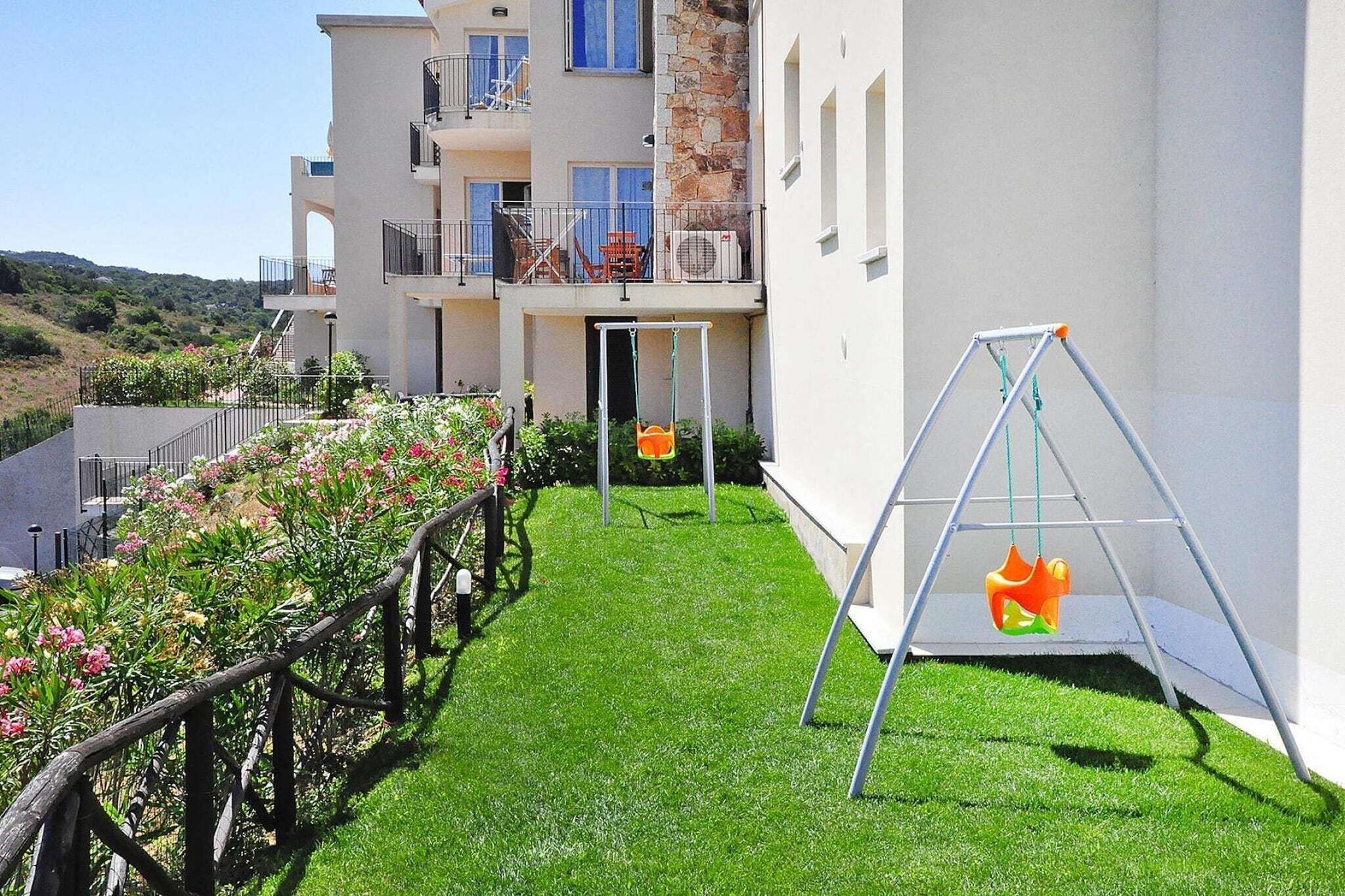 A residential building with a balcony, a swing set, and a well-maintained lawn.