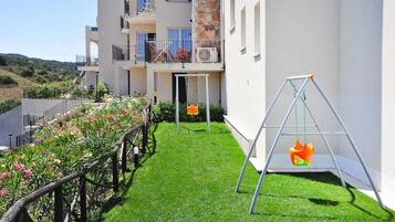 A residential building with a balcony, a swing set, and a well-maintained lawn.